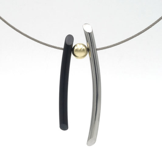 Collier met twee langgerekte hangers er aan, met een gouden balletje ertussen. De ene hanger is zwart en net iets korter dan de andere, die van glanzend edelstaal is.