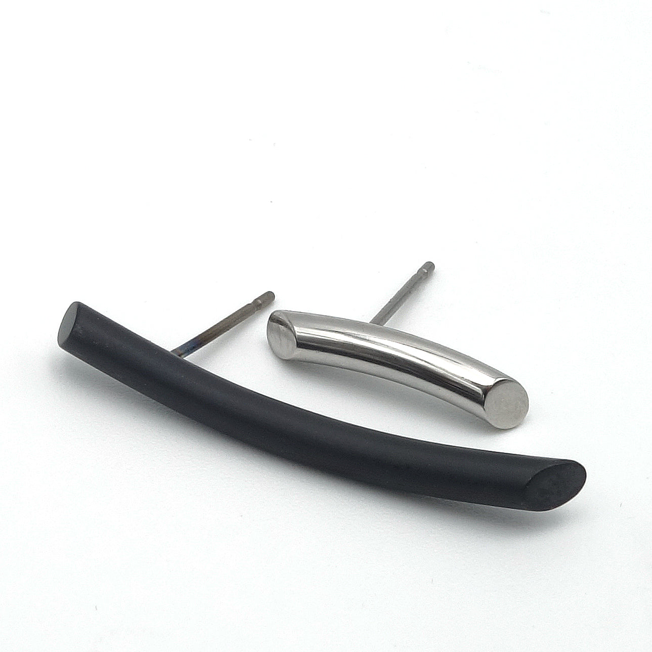 Langgerekte oorbellen, de ene langer dan de ander, de ene zwart mat metaal en de ander wit glanzend metaal.