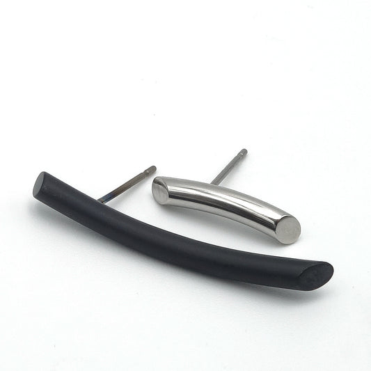 Langgerekte oorbellen, de ene langer dan de ander, de ene zwart mat metaal en de ander wit glanzend metaal.