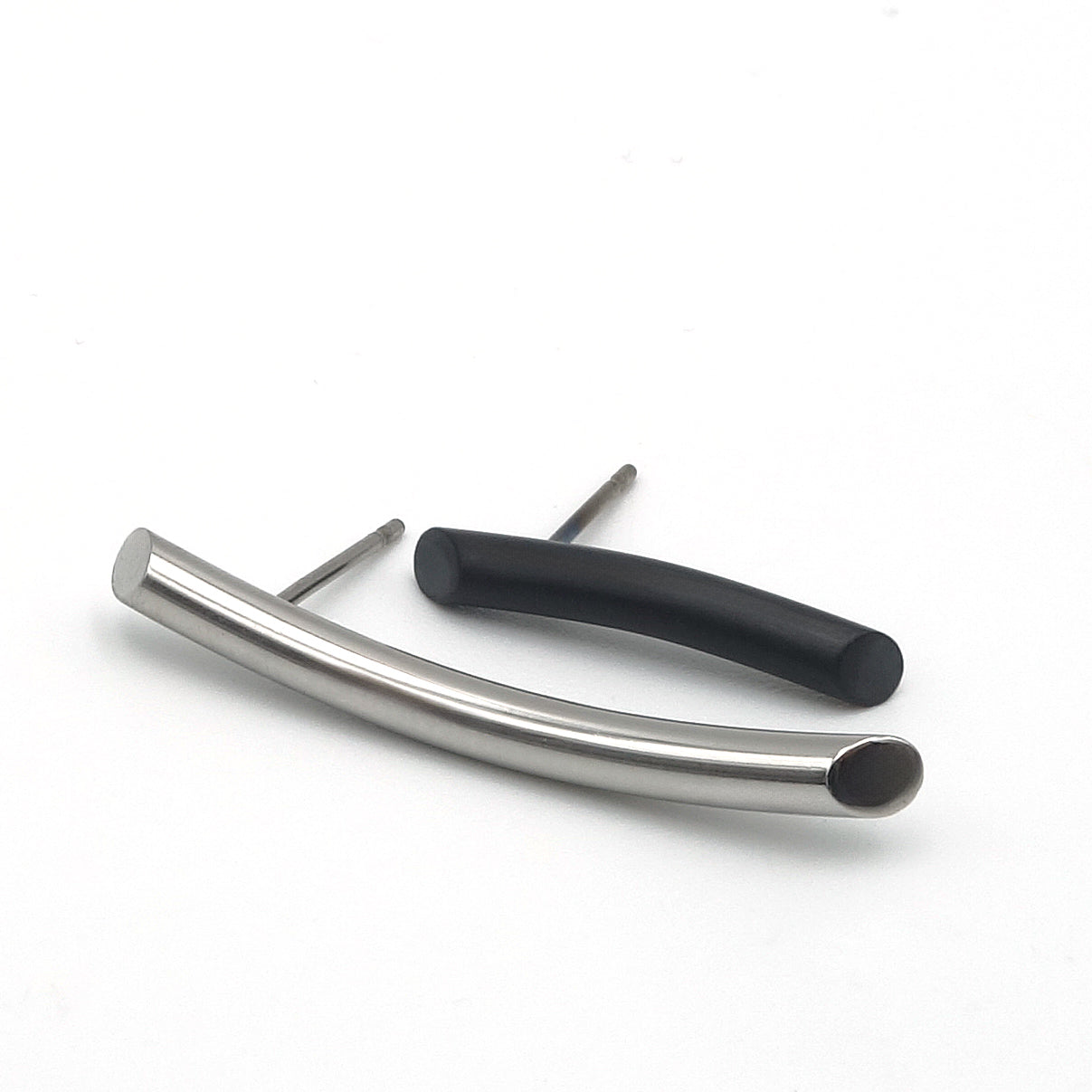Twee verschillende oorbellen van licht gebogen metalen staafjes. De ene is lang en van glanzen edelstaal, de andere is kort en van mat zwart zirkonium