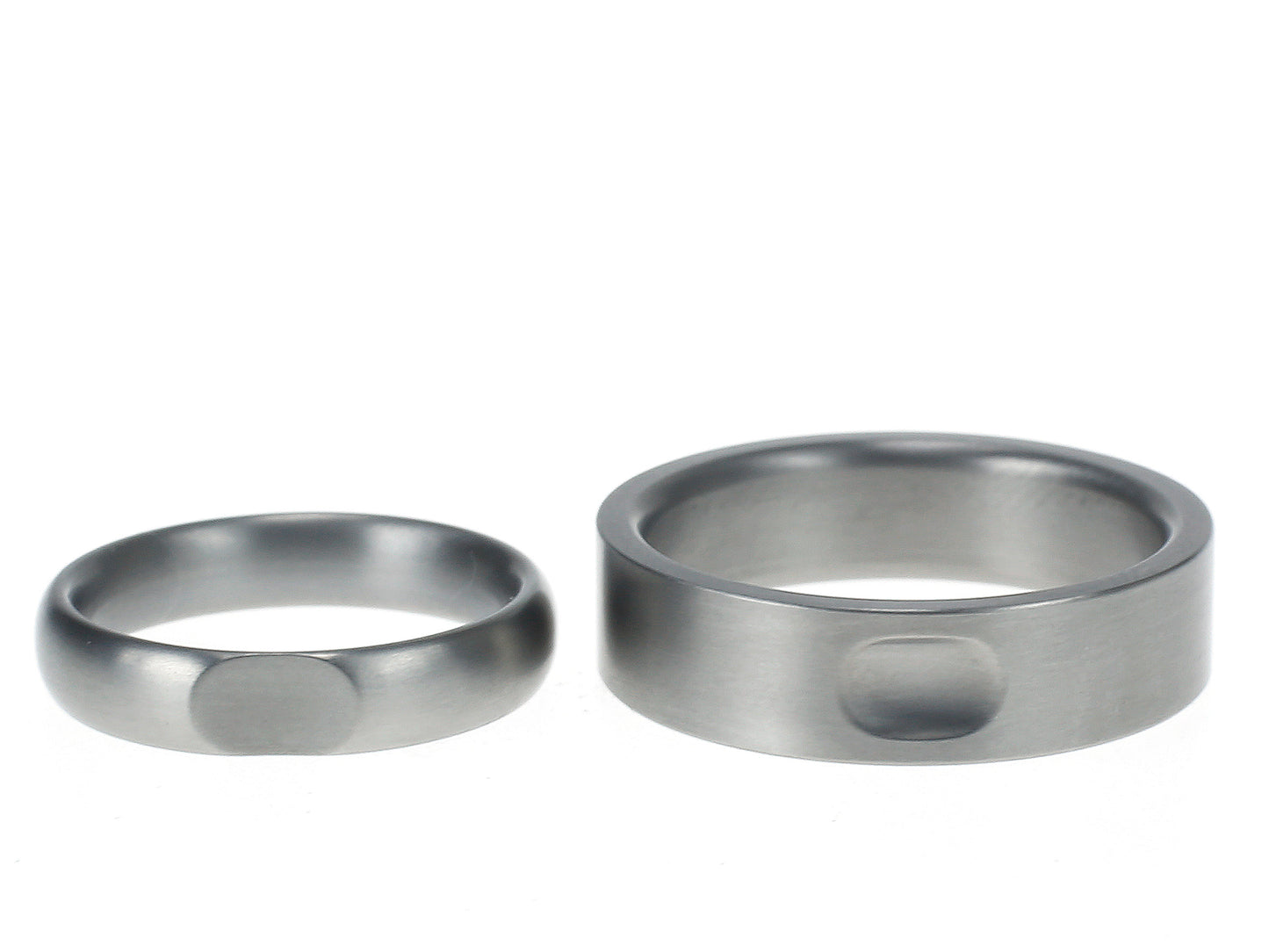 Twee titanium ringen met bijpassende inkepingen die elkaars vorm weerspiegelen – een strakke vlakke ring en een bolle variant.