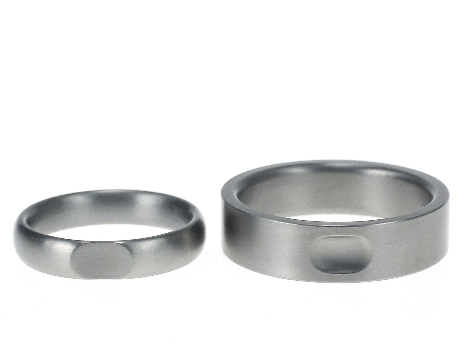 Twee titanium ringen met bijpassende inkepingen die elkaars vorm weerspiegelen – een strakke vlakke ring en een bolle variant.