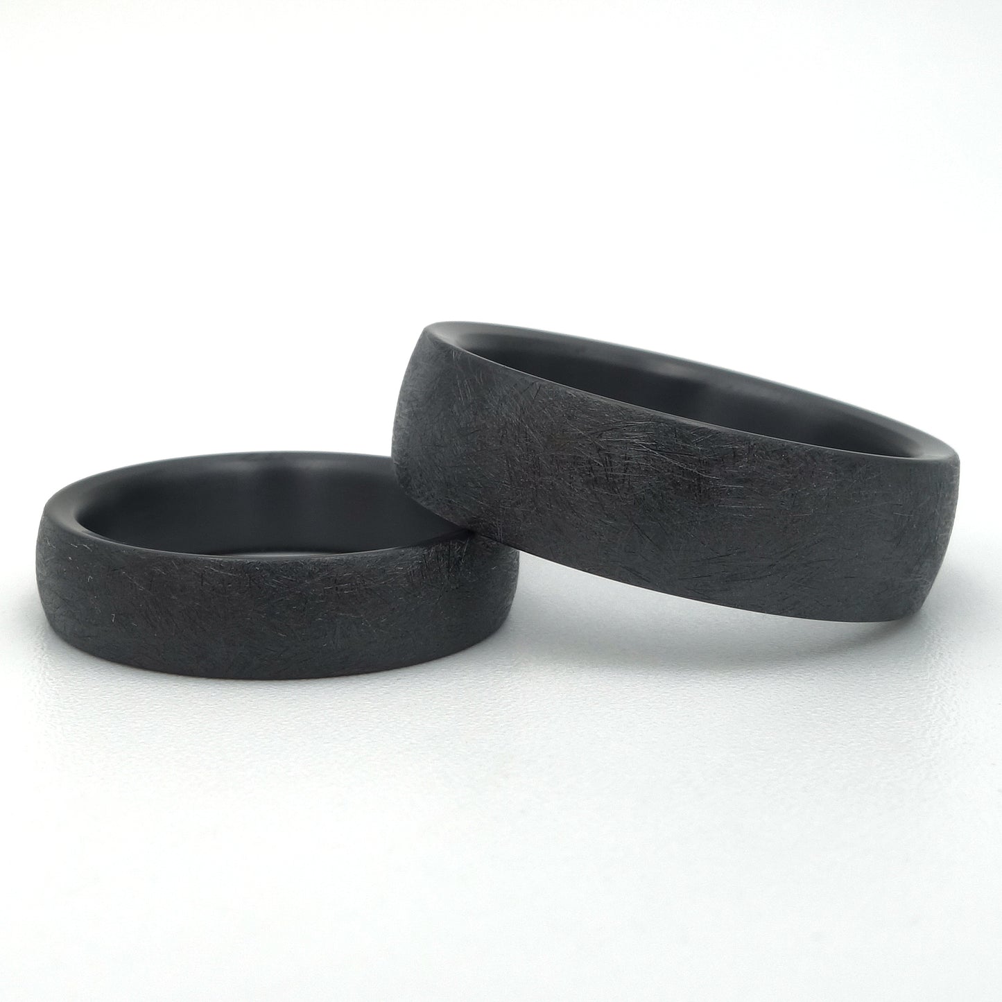 Twee zwarte zirkonium ringen met gekraste oppervlaktetextuur, 5mm en 7mm breed, mat afgewerkt.