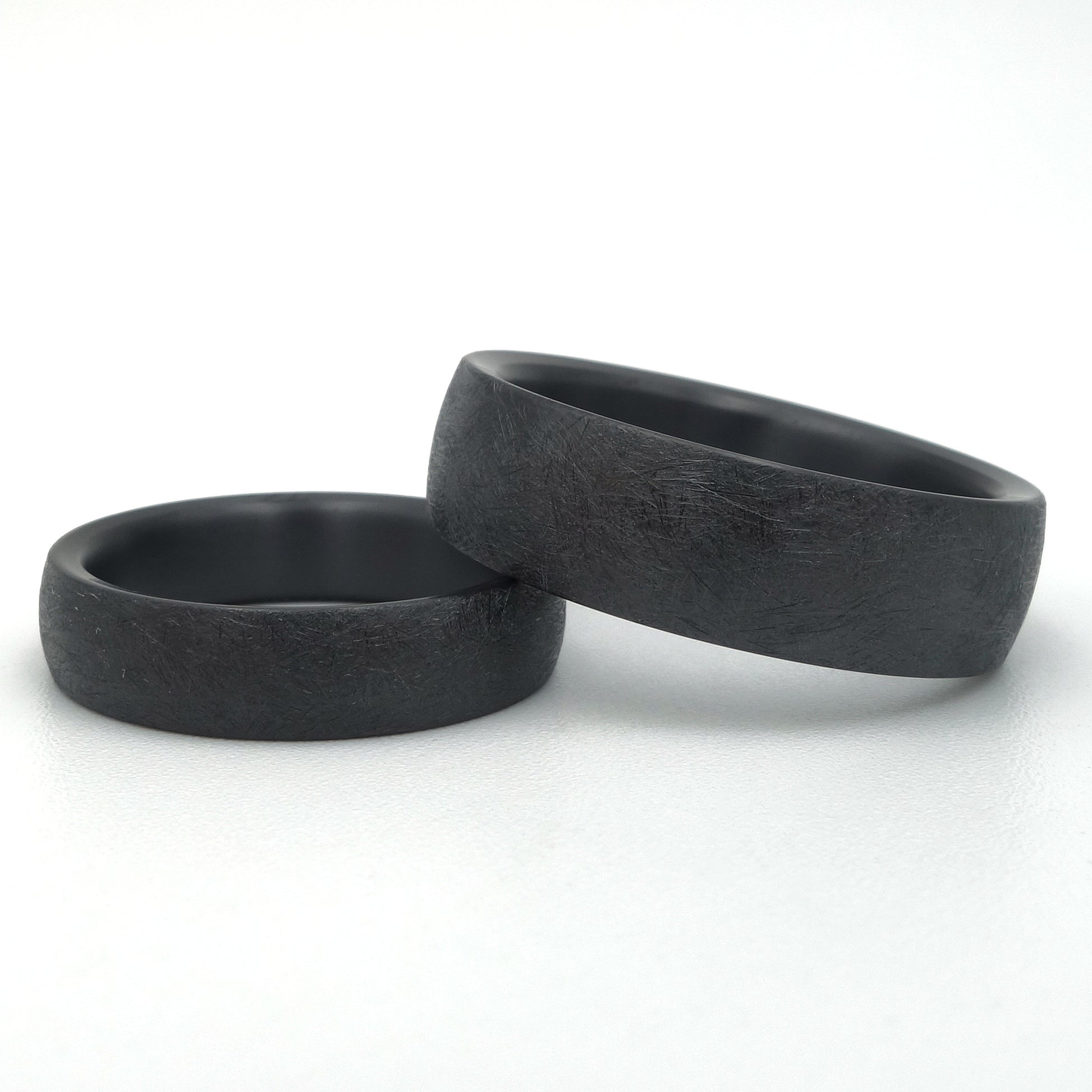 Twee zwarte zirkonium ringen met gekraste oppervlaktetextuur, 5mm en 7mm breed, mat afgewerkt.