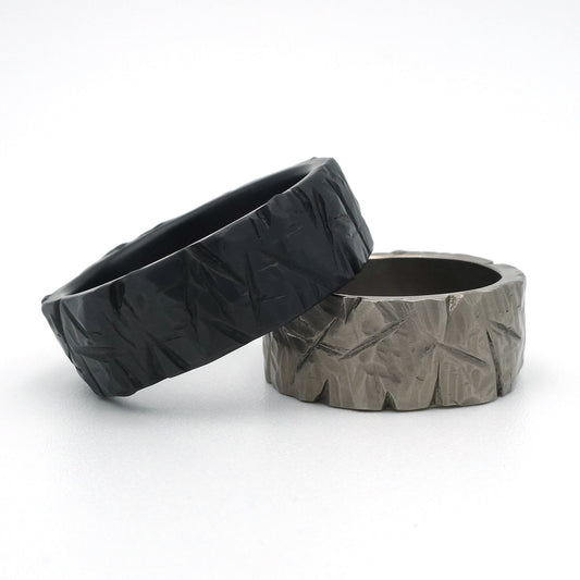 Set Smashed ringen, 8,5 mm breed, in zwart zirkonium en grijs titanium met grof geslagen patroon.