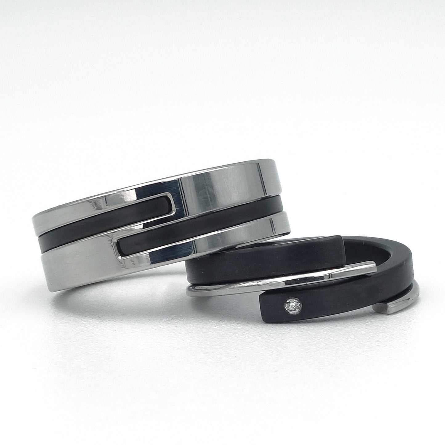 Moderne trouwringen: brede edelstalen ring met zwarte inleg (zirkonium) en smalle zwarte ring (zirkonium) met stalen zijring en diamant – Adam & Eva in staal en zwart.