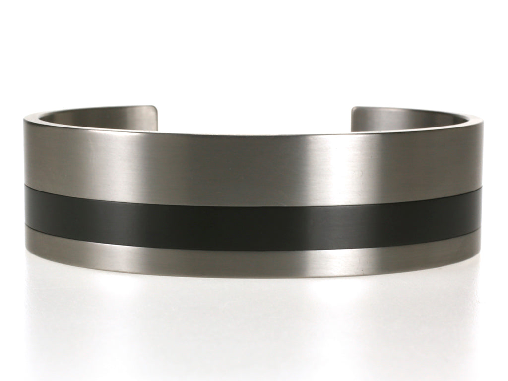 Brede armband van titanium met zwarte zirkonium inleg, gefotografeerd op een witte achtergrond.