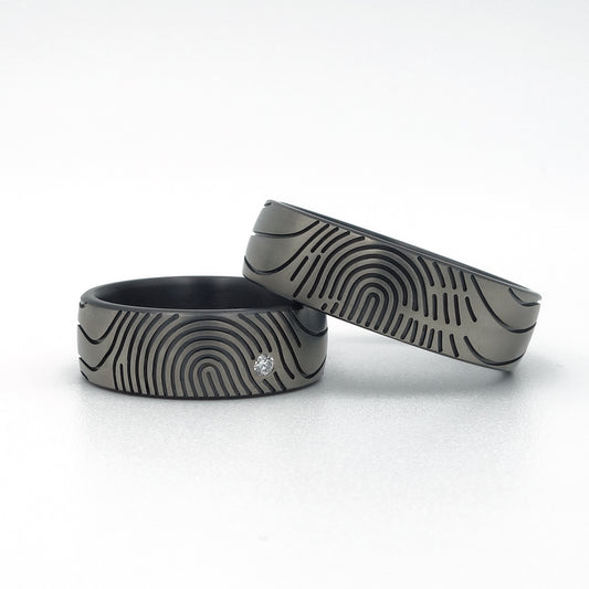 Twee moderne zirkonium trouwringen met vingerafdrukdesign, waarvan één met diamantaccent.