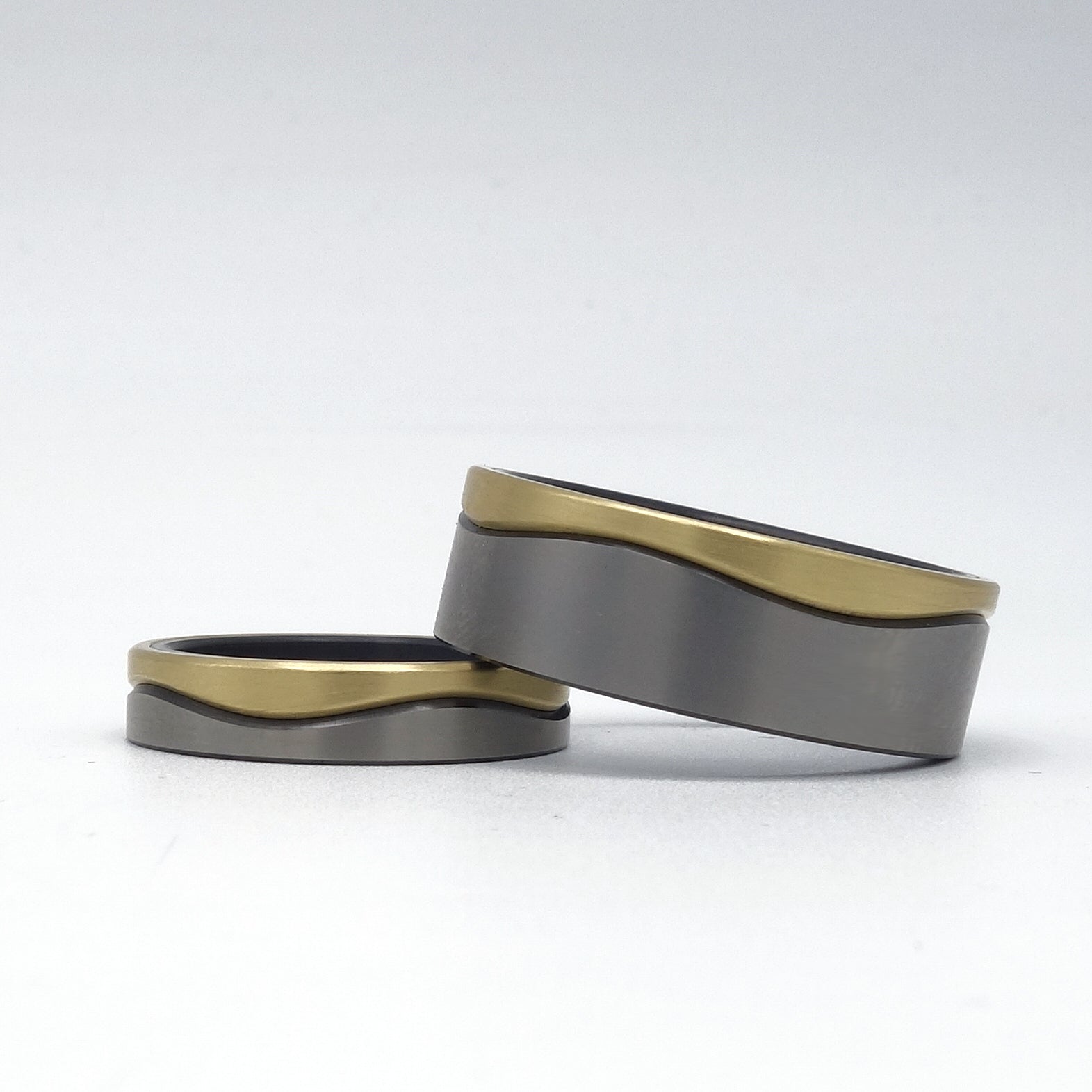 Twee trouwringen met dunne golvende lijn in 14 karaat geelgoud op een basis van zwart zirkonium, in 4,5 mm en 8 mm breedte.

