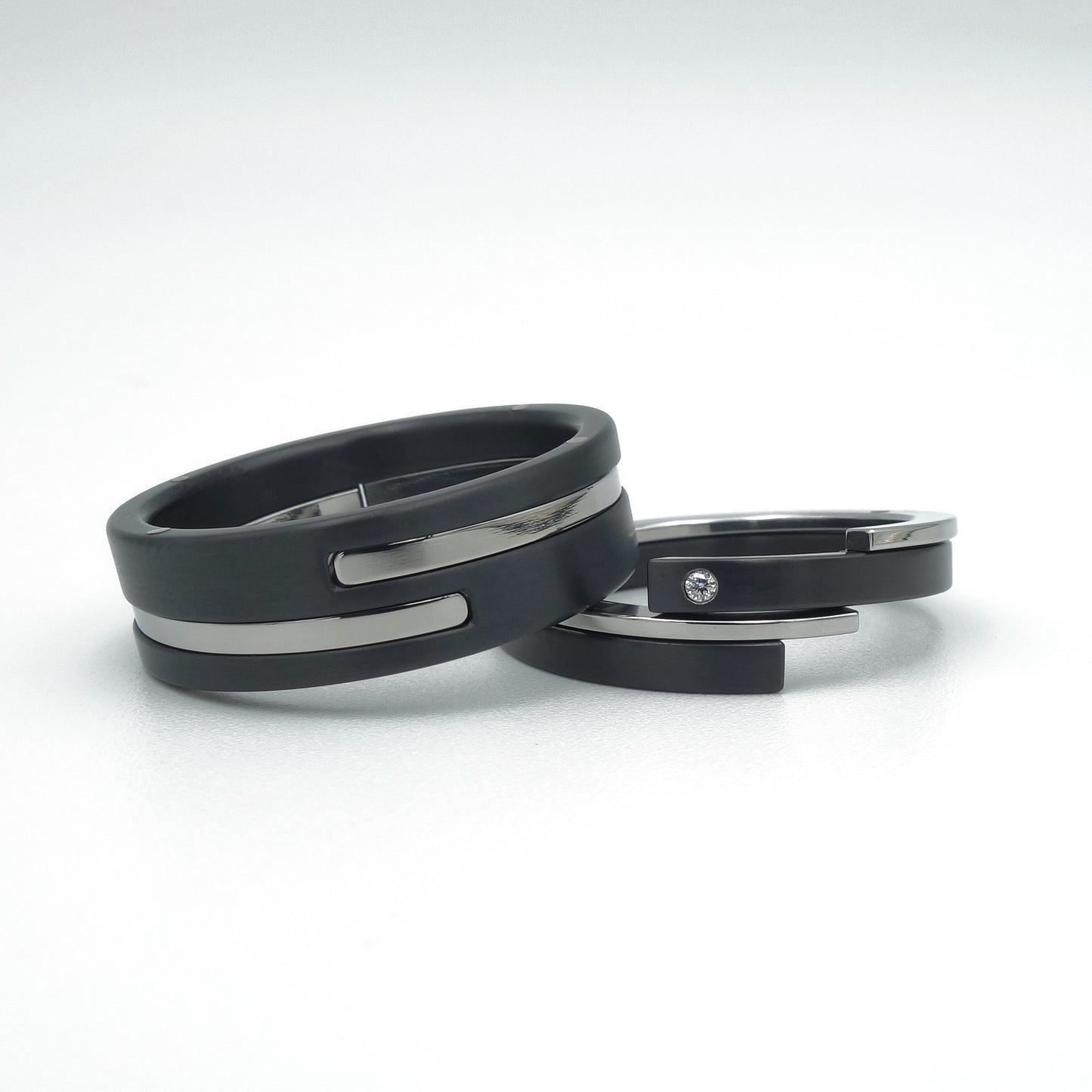 Twee ringen met modern design: brede ring in zwart zirkonium met edelstalen inleg, smalle ring met diamant. Symbolische set trouwringen.