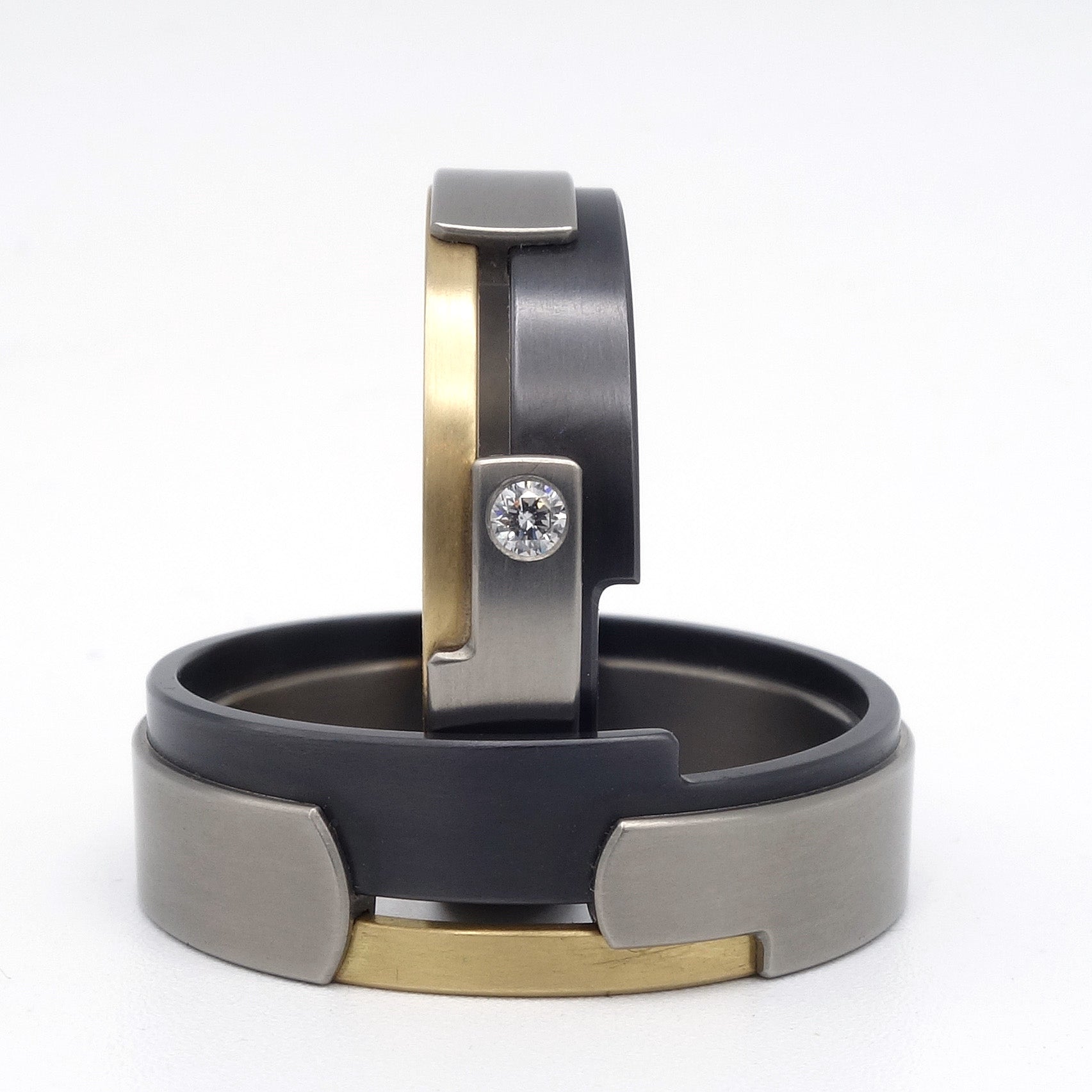 Aquila ringenset van geelgoud, titanium en zirkonium – gelaagd ontwerp met modern contrast en diamantaccent in de damesring.

