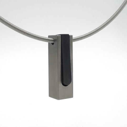 Tweedelige blokhanger van titanium met los binnendeel van zwart zirkonium aan stalen spangketting