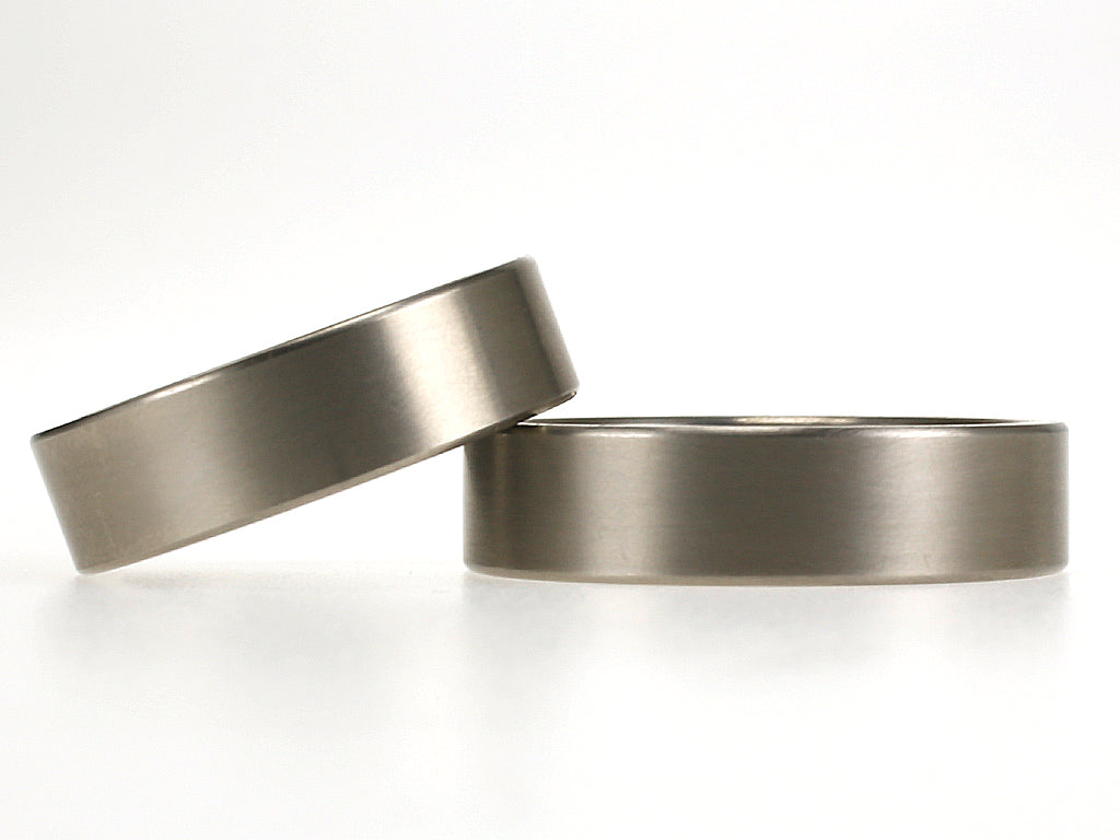 Eenvoudige titanium trouwringen met rechte vorm en matte afwerking, beide 6 mm breed.