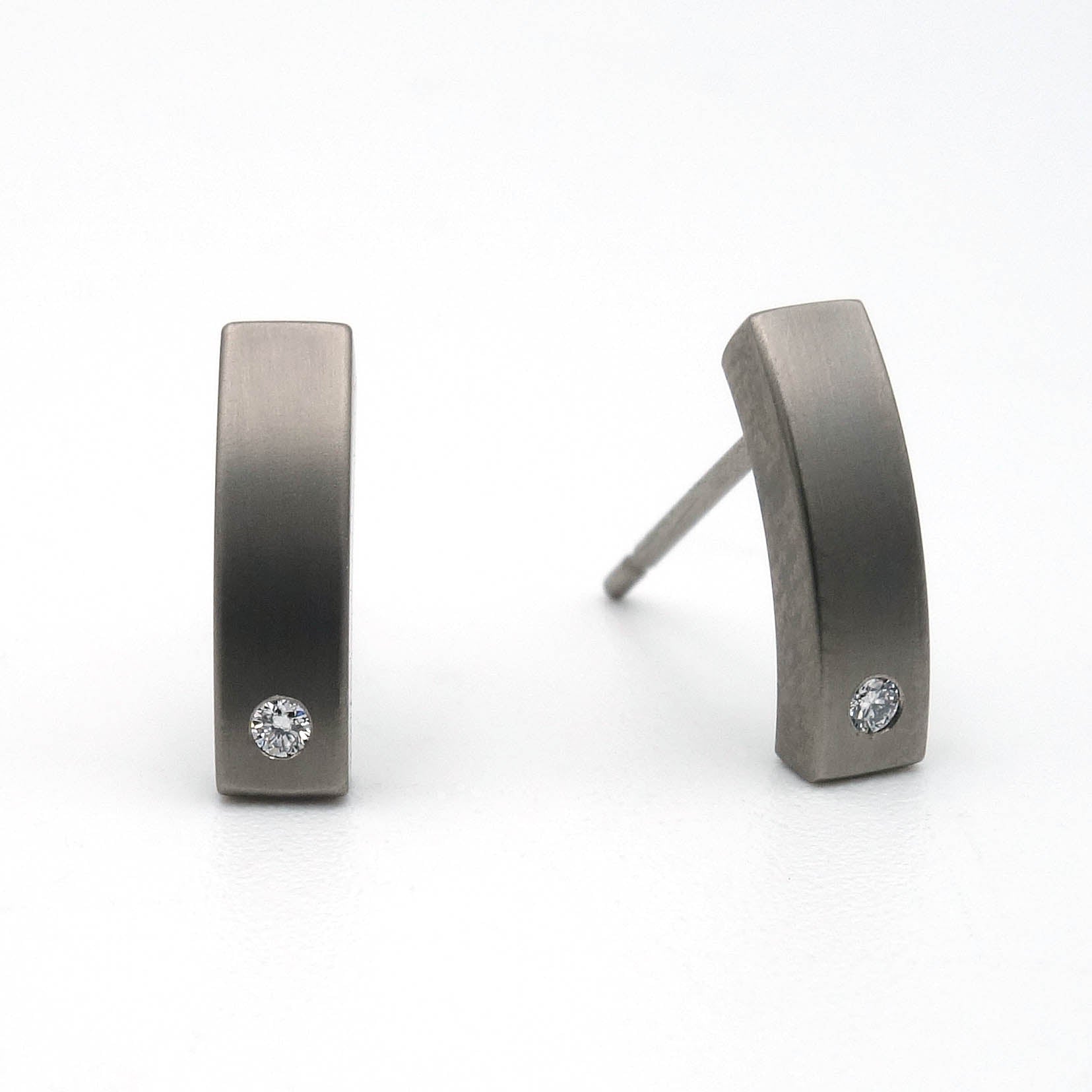 Titanium oorstekers met geborstelde afwerking en kleine briljant geslepen diamant aan de onderzijde, gefotografeerd tegen een witte achtergrond.