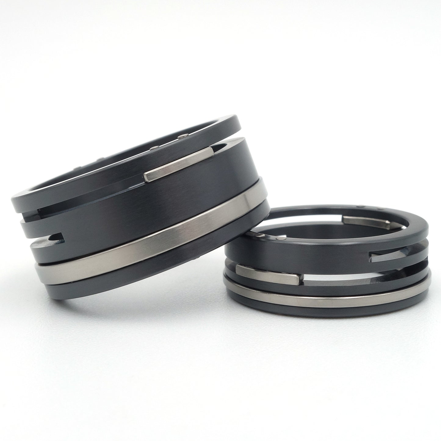 Twee zwarte zirkonium en titanium ringen met horizontale gleuven en witgouden klinknagels, 10mm en 7mm breed.