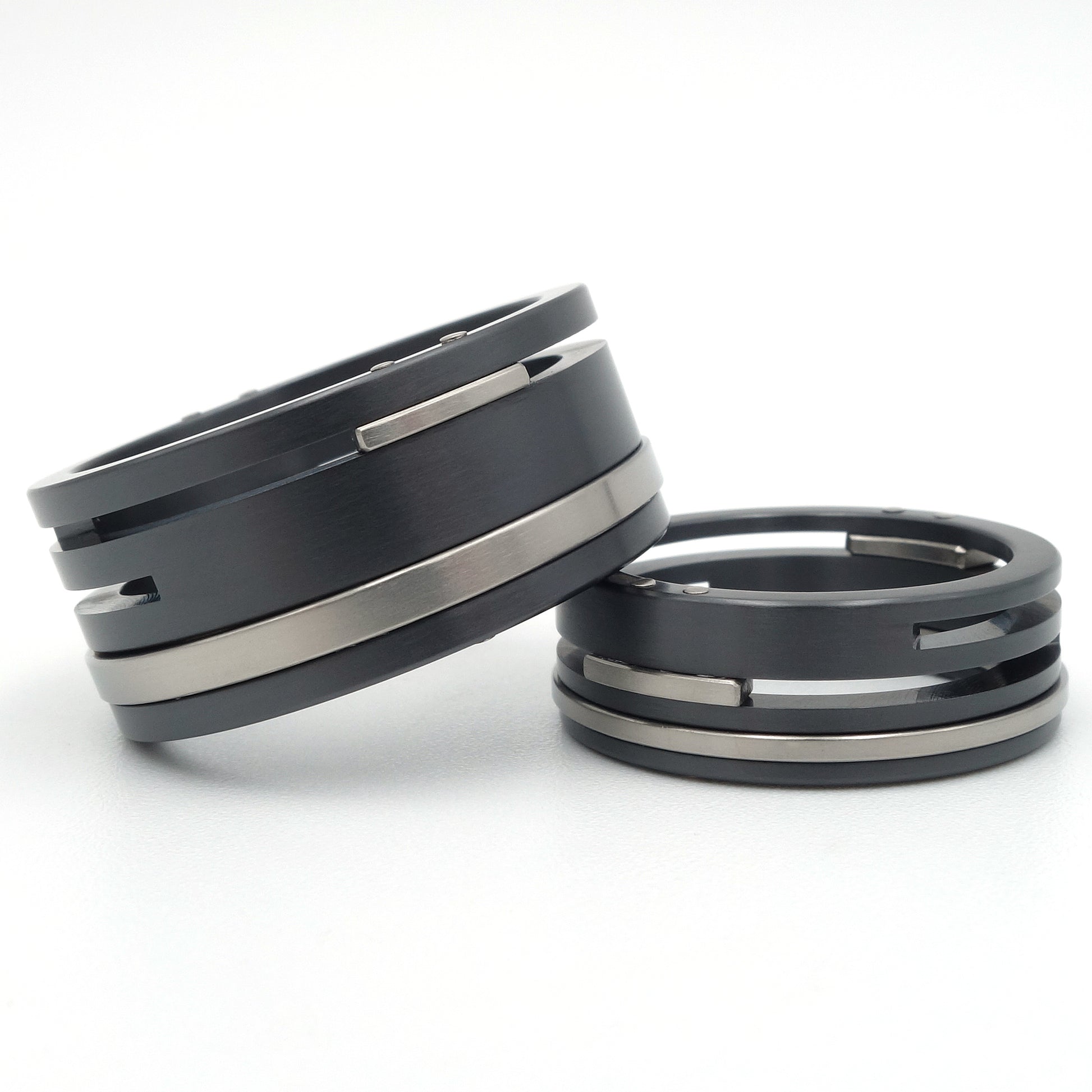 Twee zwarte zirkonium en titanium ringen met horizontale gleuven en witgouden klinknagels, 10mm en 7mm breed.