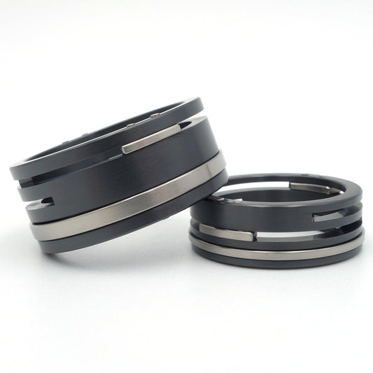 Twee zwarte zirkonium en titanium ringen met horizontale gleuven en witgouden klinknagels, 10mm en 7mm breed.