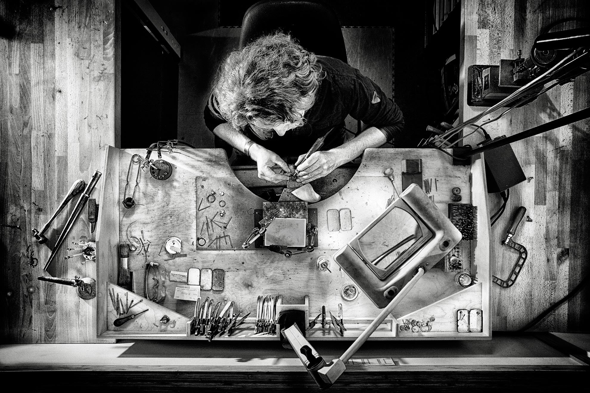 Joeri Dijkman aan het werk aan zijn goudsmid werkbank – bovenaanzicht in zwart-wit van het ambachtelijke sieradenatelier.

