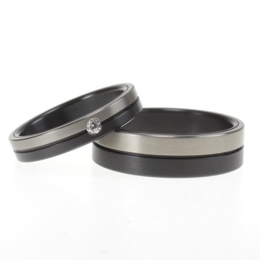 Set zwart-witte trouwringen met titanium bovenlaag; één ring met diamant, de ander zonder.

