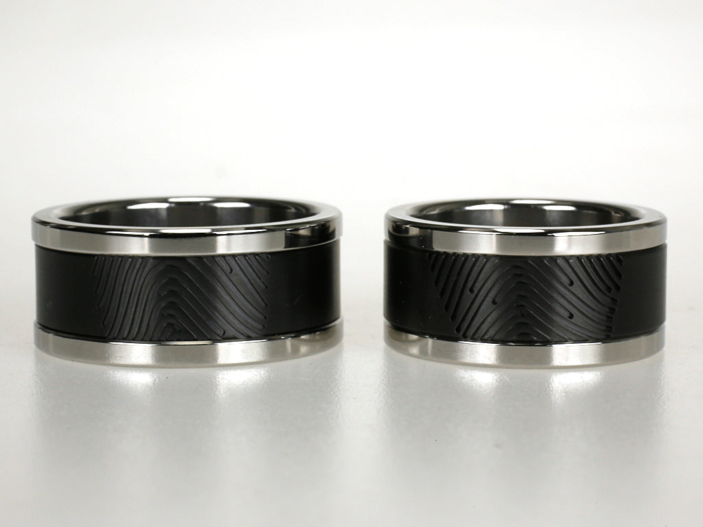 Stoer ring van zwart zirkonium met vingerafdruk en hoogglanzende titanium randen.